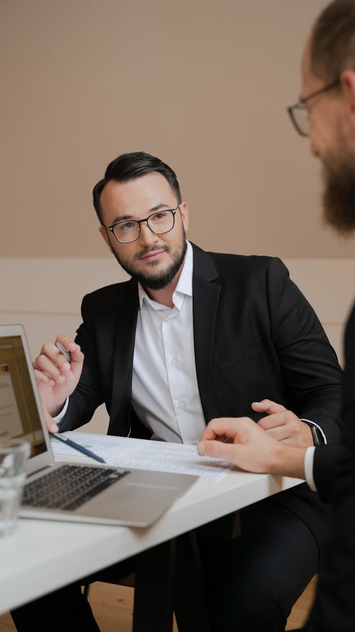 Two businessmen in a meeting discussing strategies with laptops and documents.
